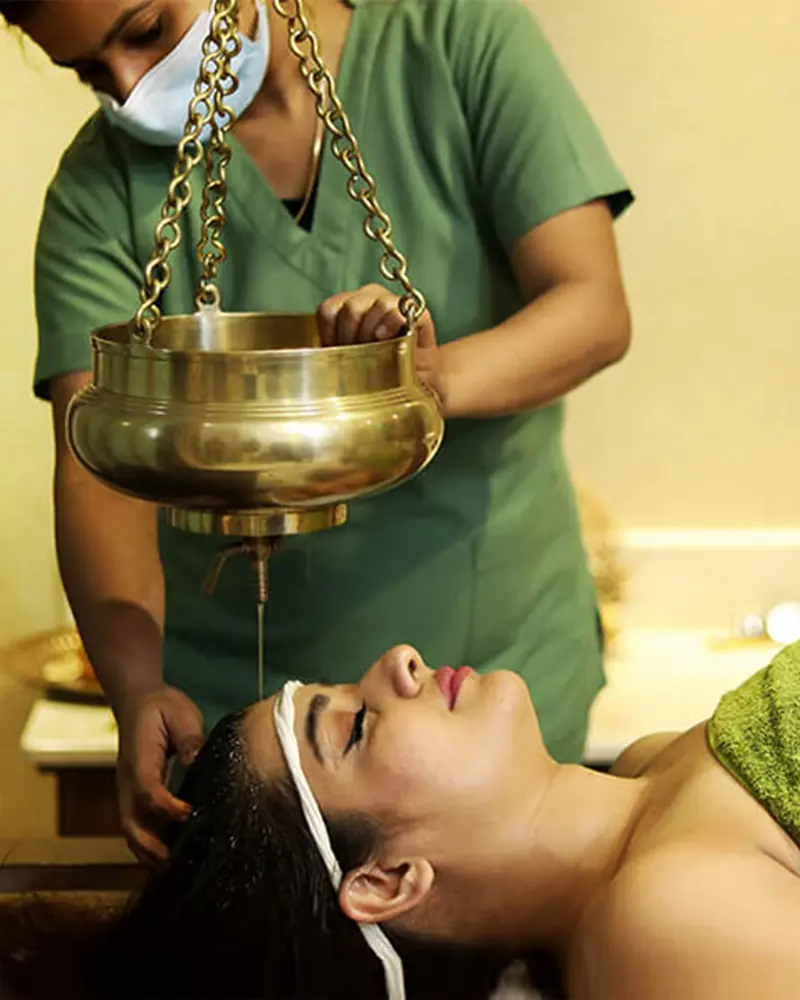A therapist pouring warm oil for a Shirodhara treatment
