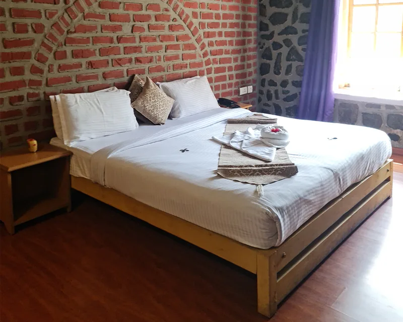 A bedroom in the pool villa, king bed against a brick arch with stone walls and a window onto the trees