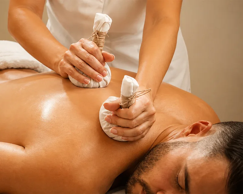 A therapist working with warm herbal poultices across a guest’s back